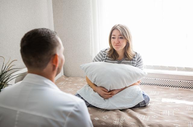 woman on bed holding pillow, facing man